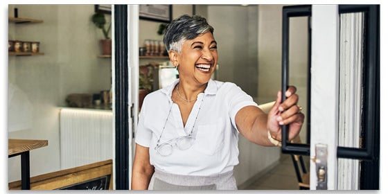 Smiling woman opening the door to her retail business.