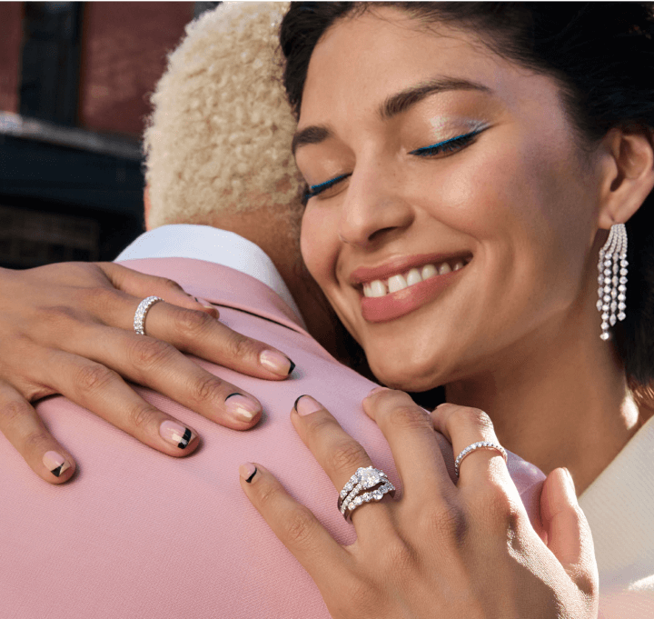  A woman joyfully hugs a man, showcasing beautiful diamond rings and Earrings.