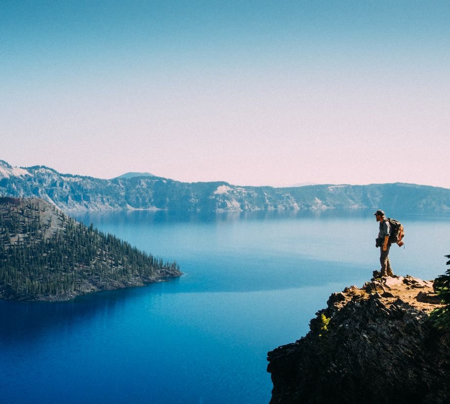 A fella stands atop a cliff looking out across a giant lake and distant lands.