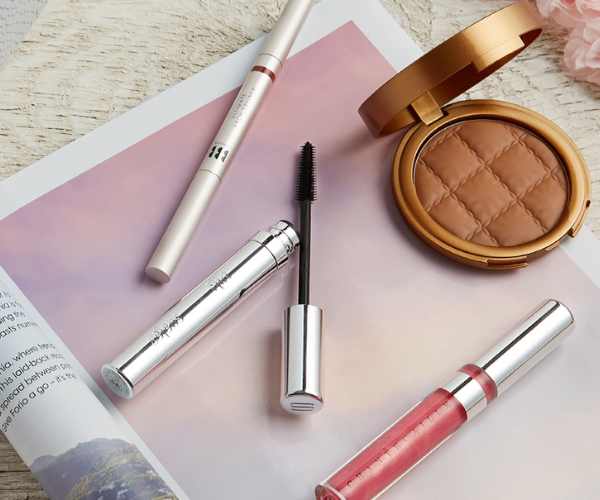 Makeup products lay on top of a magazine on the beach