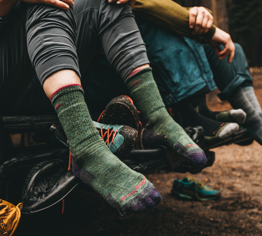 A group of hikers sits on the back of a truck, unleashing their cozy Darn Tough socks from soggy sneakers.