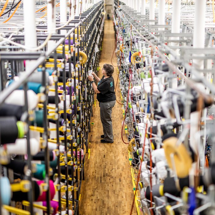 A visit to the mill - a Darn Tough employee standing between two walls of yarn spools at our Vermont mill.