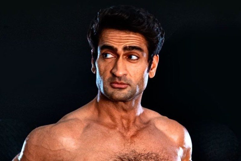 a ripped Kumail Nanjiani shirtless with his hands on his hips in dark gym