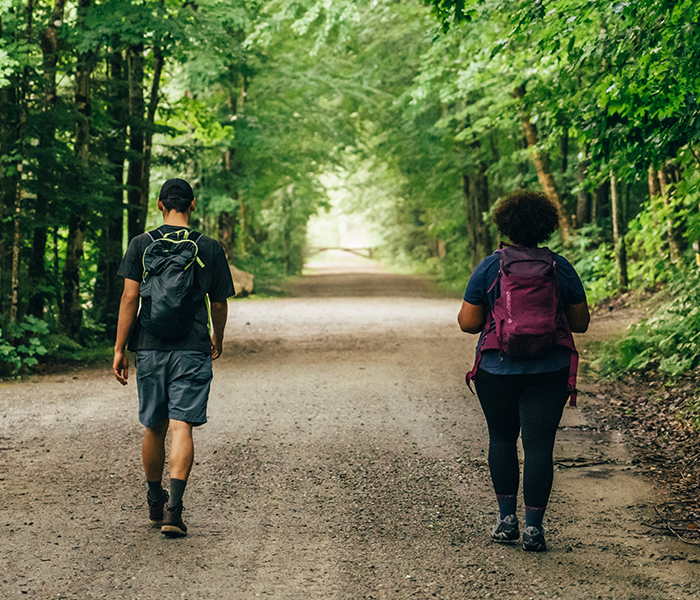 Two young people with backpacks walk along a dirt road, appropriately socially distanced. 