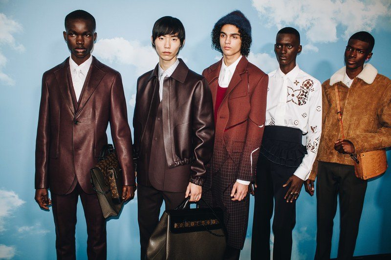 a group of male models wearing louis vuitton in front of wall with sky and clouds wallpaper on it
