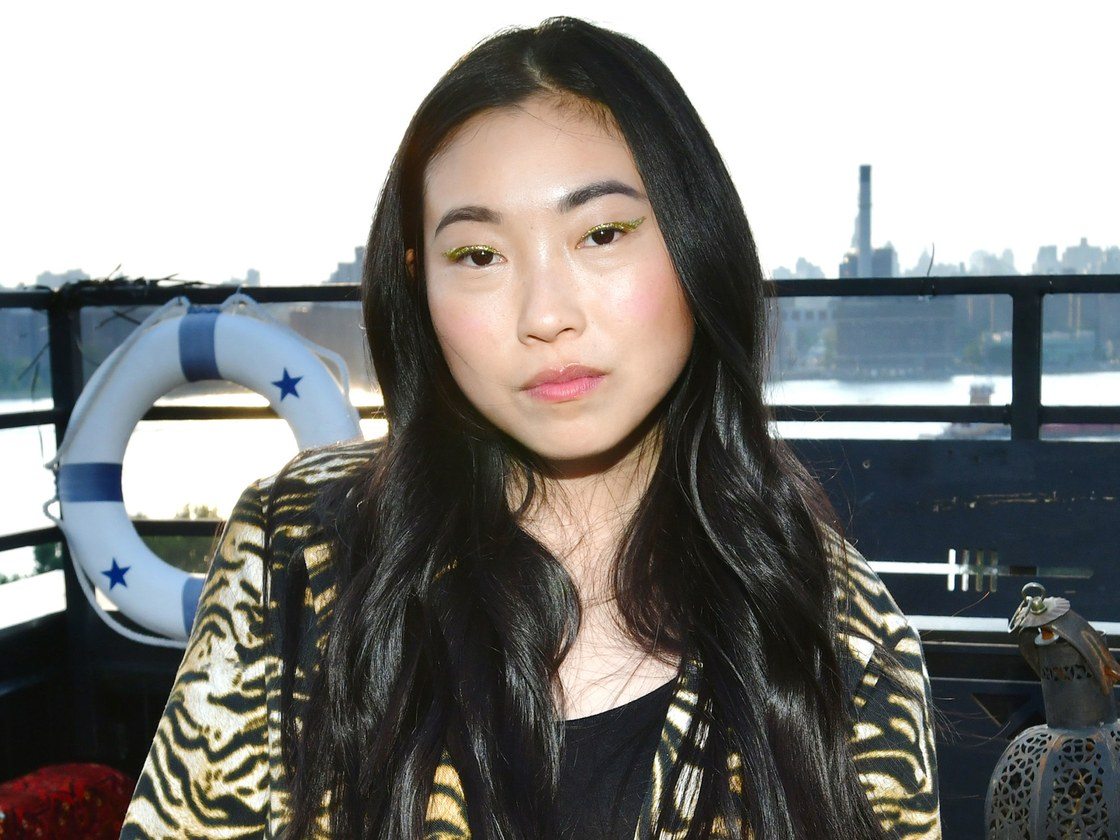 Awkwafina wears an animal print coat with a black tank top and gold eye shadow