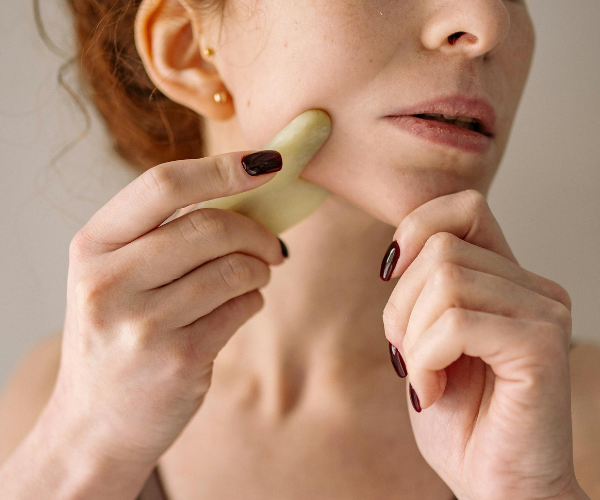 Woman gliding gua sha tool across her jawline.