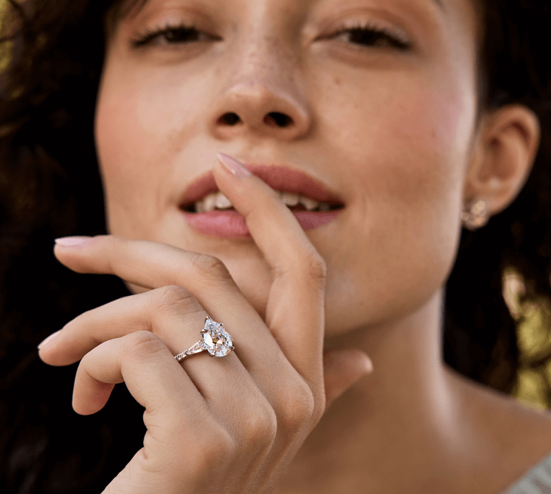 A woman poses playfully, with a beautiful Bridal ring prominently displayed.