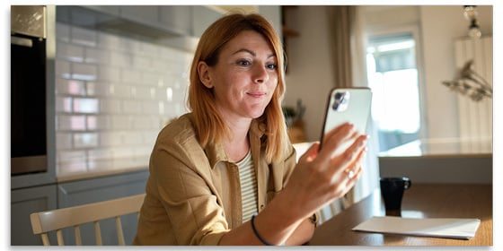 Smiling woman looking at her mobile phone while sitting at a table.