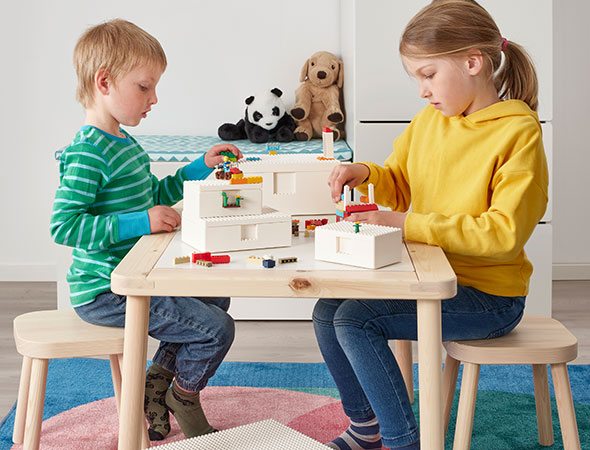 Two children play with LEGO bricks together at a wooden table