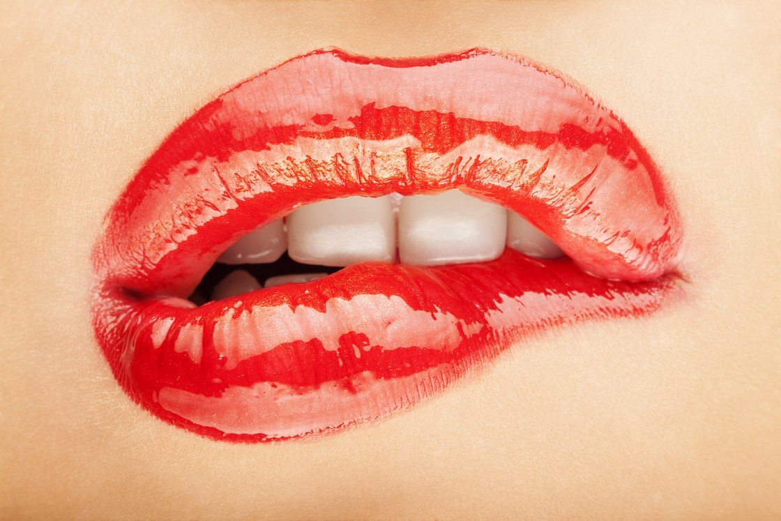 A pair of glossy red lips being bitten.