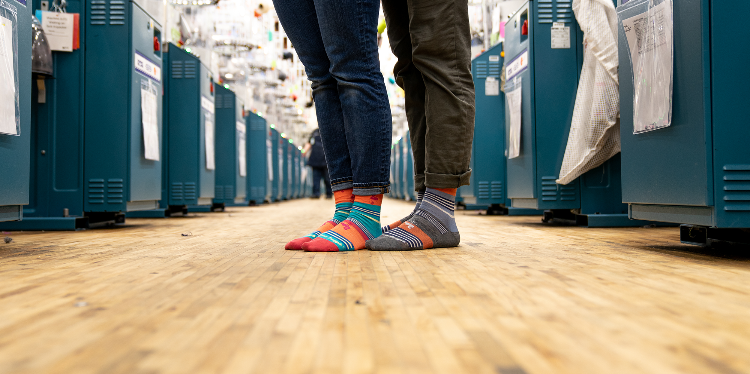 Two pairs of feet dressed merino wool socks, nested together on the floor of a sock production mill in beautiful Northfield, Vermont