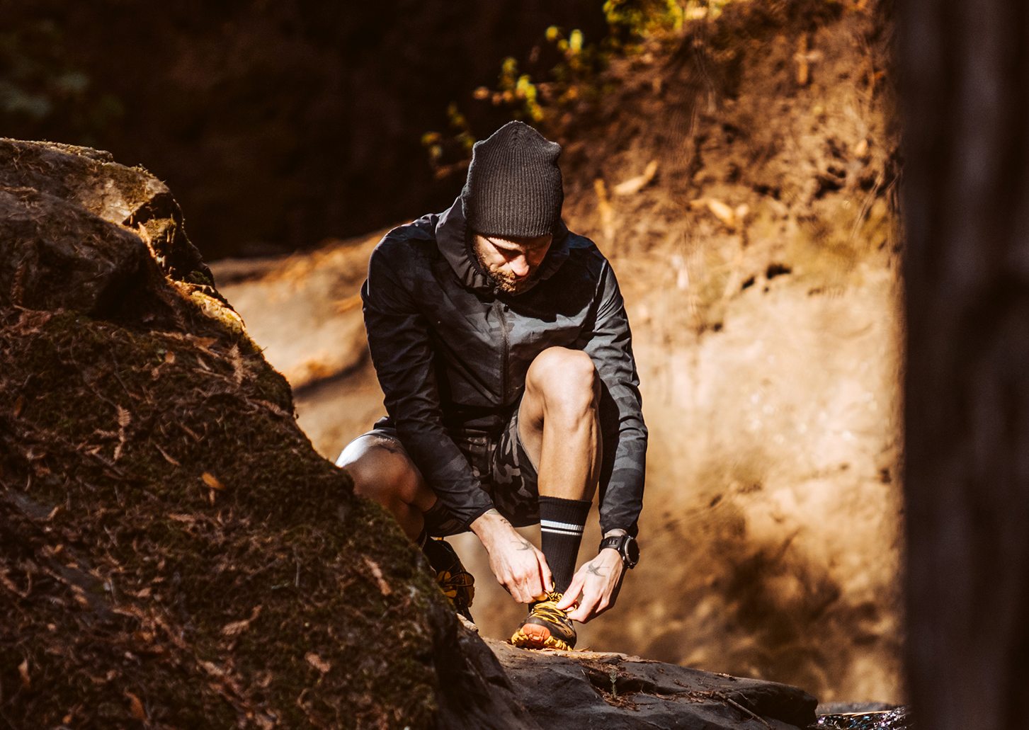 A man squat to adjust his shoe, a glorious sock catches the canyon sun.