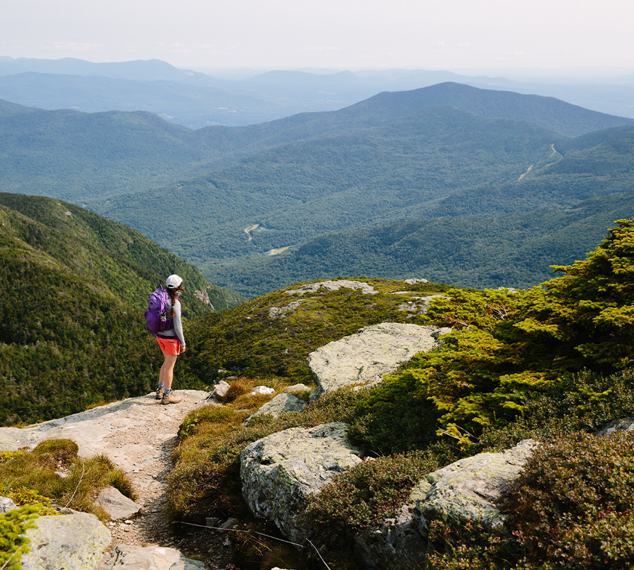 A backpacker rocking bright shorts and even cooler socks gazes over a vast mountain range.