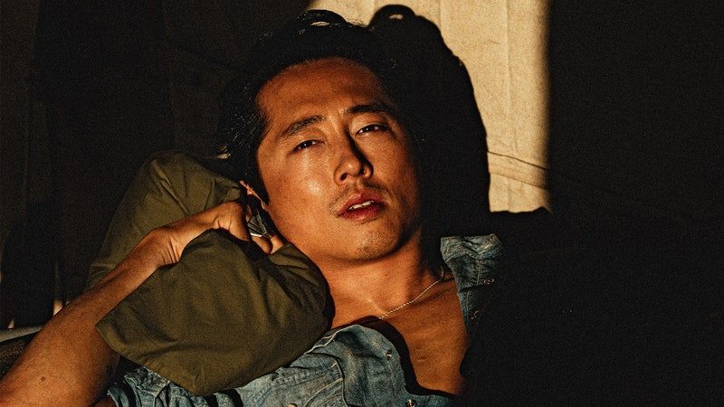 Image may contain: Steven Yeun, Human, Person, Wood, Sitting, Clothing, and Apparel