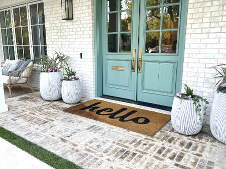 Winston Porter Caralysia Hello Outdoor Door Mat with Hello written in black on a brown mat set on white washed brick in front of teal double front doors