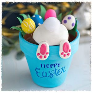 Blue easter flower pot with multicolored eggs and white easter bunny rump poking out with bunny feet