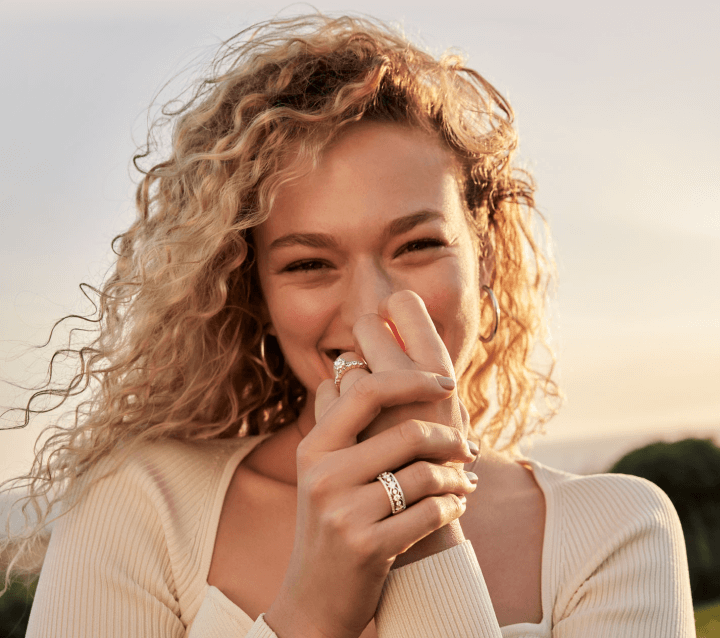 A vibrant woman poses playfully, showcasing her new anniversary & wedding rings. 