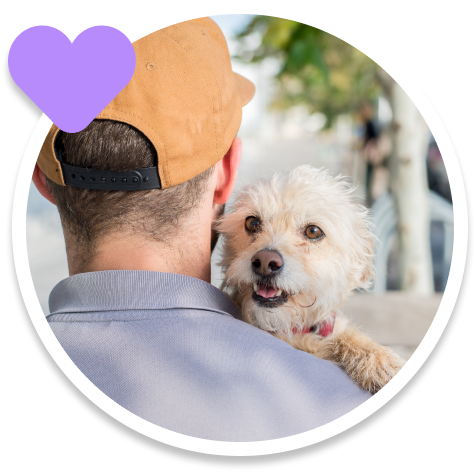 A man in a cap holds a happy white terrier mix over his shoulder.