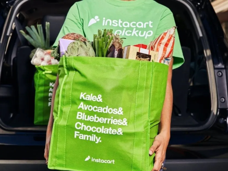 Instacart Worker holding a green Instacart tote bag with groceries inside of it