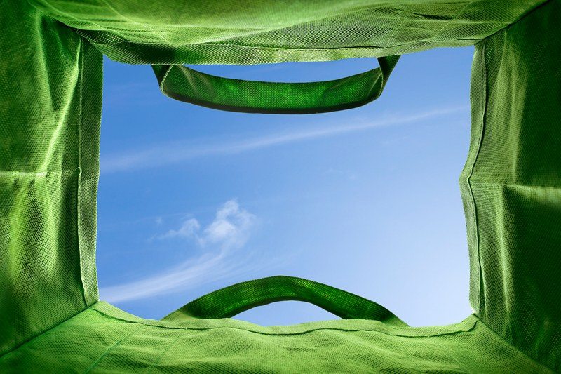 View from the bottom of a reusable green bag, looking up at a blue sky