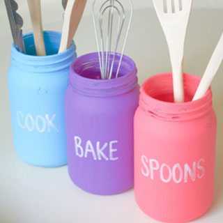 3 painted canning jars with words in blue (cook), purple (bake), and pink (spoons)