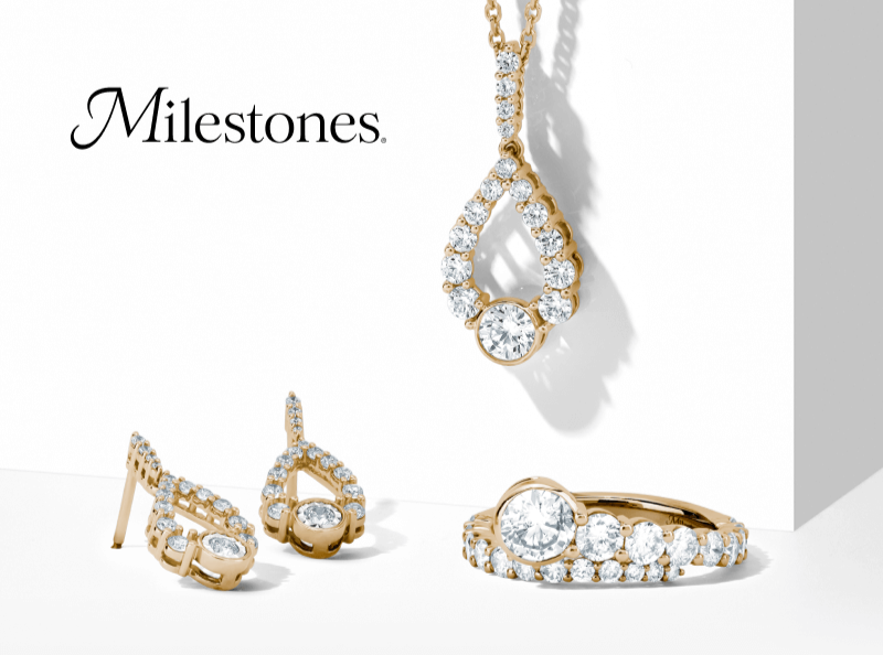 A display of gold and diamond Milestones jewelry, including earrings, necklace, and ring