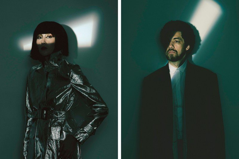 Musicians Karen O and Danger Mouse standing in a ray of light against a blue background