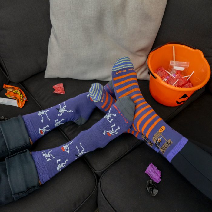 Feet up on the couch next to candy wearing halloween socks featuring dancing skeletons and black cats