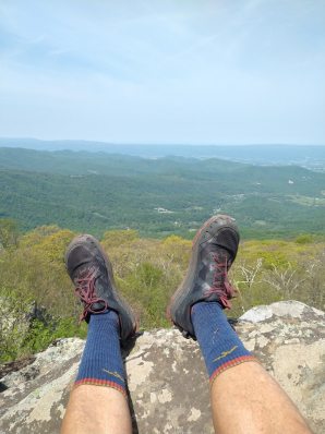 A hiker stretches out their feet while sitting on a mountain summit, showing off their blue Darn Tough socks