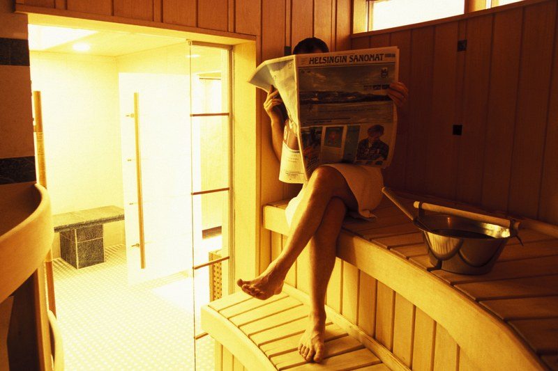 a man sitting in a sauna reading a newspaper
