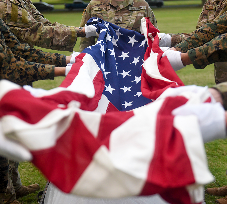 A group of servicemembers lay an American flag over a fallen hero.