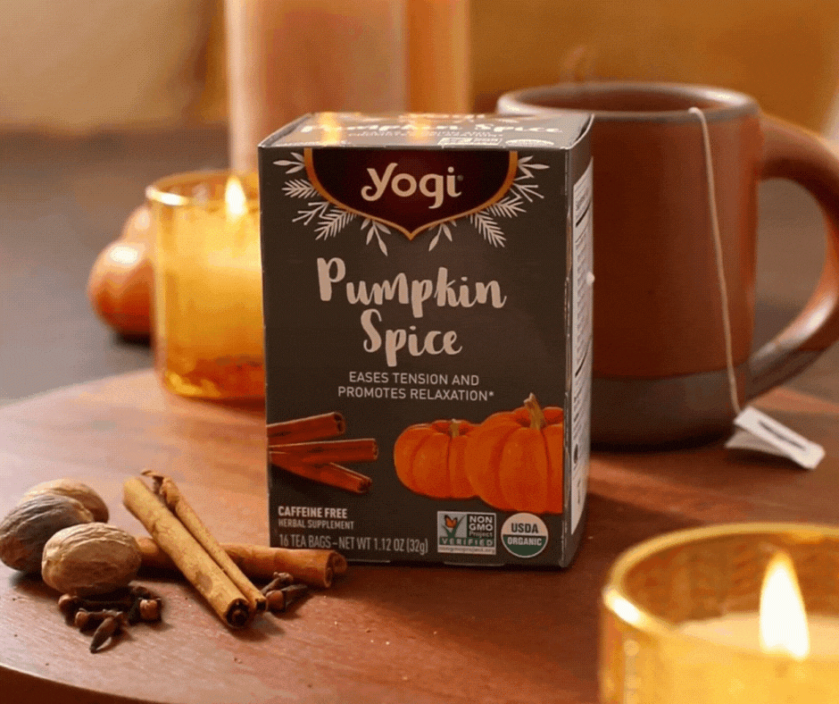 Yogi's Pumpkin Spice Tea sits on a wooden serving board, next to Cinnamon sticks, Clove, some candles, and a mug of tea.