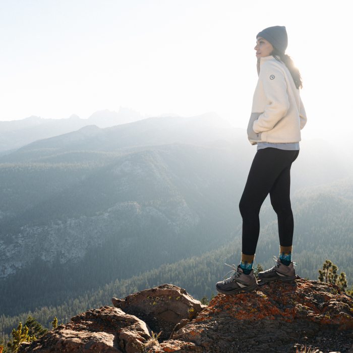 Shop warm hiking socks - a hiker stands at the top of a summit, bundled up and unbothered by the cold