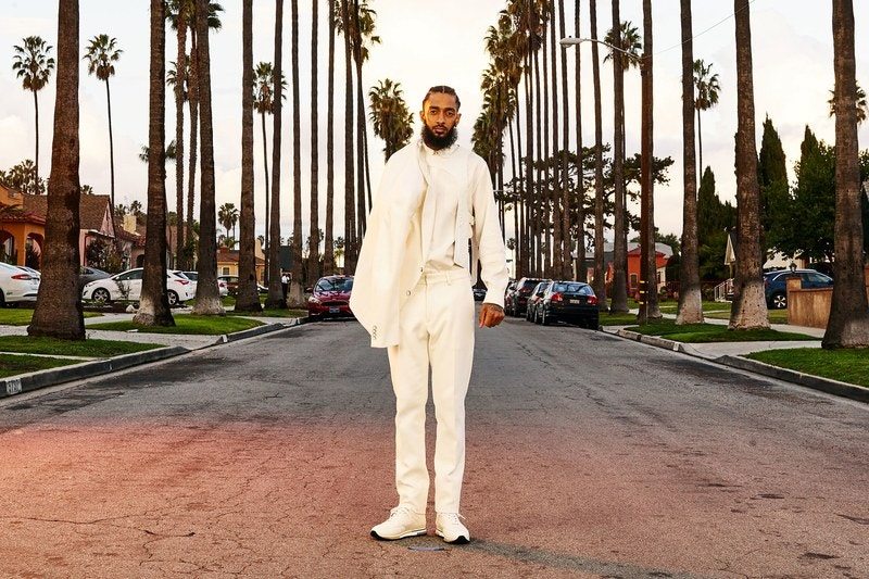 This image may contain Clothing, Apparel, Human, Person, Coat, Tree, Plant, Palm Tree, Arecaceae, Overcoat, and Nipsey Hussle