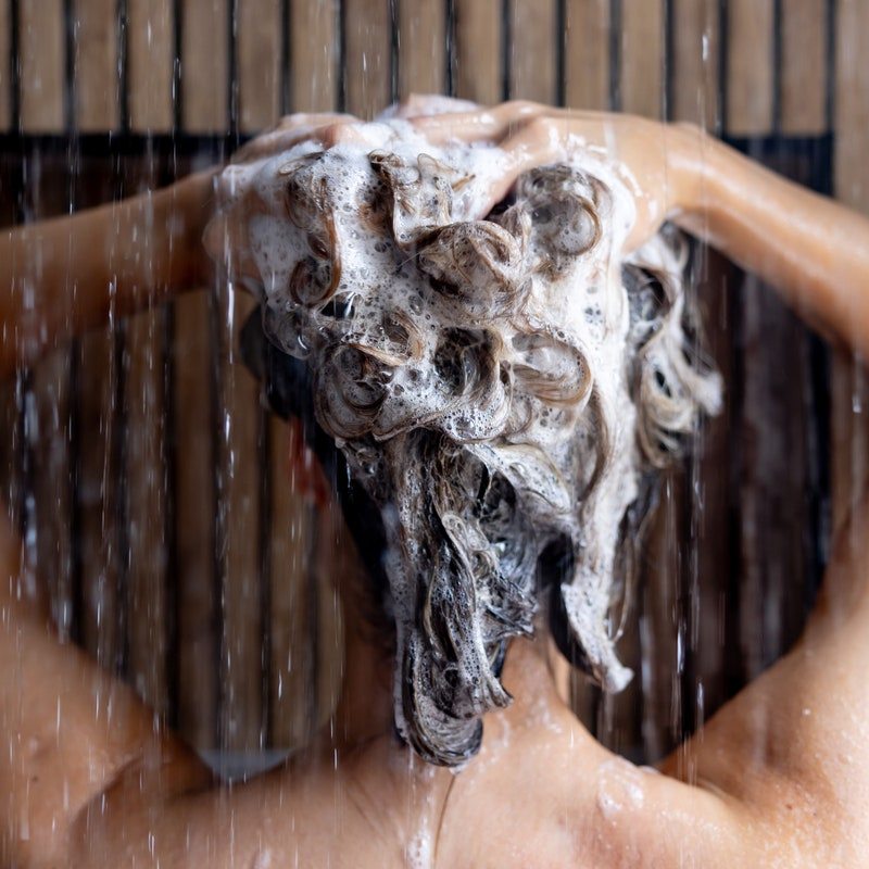 Rear view of a woman washing her hair with shampoo in the shower - morning routine concepts