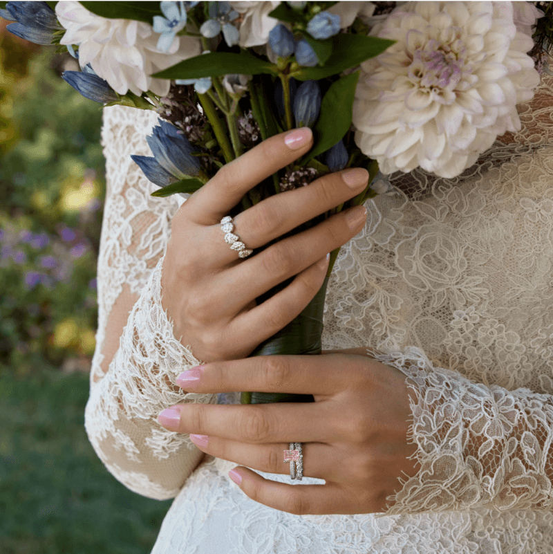 A bride holds a Bouquet of flowers, wearing two beautiful bridal rings.