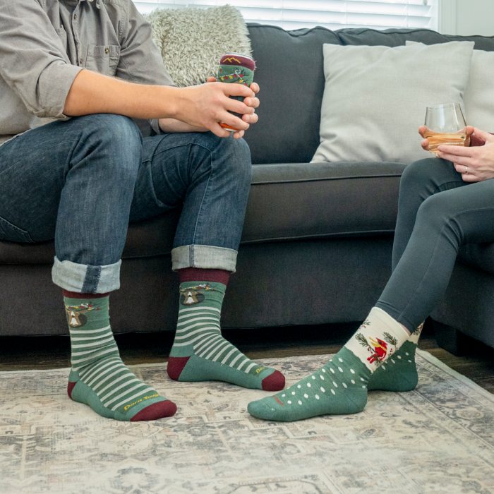 Shop limited edition holiday socks - Two people conversing on a couch, wearing green Darn Tough socks with animal patterns.