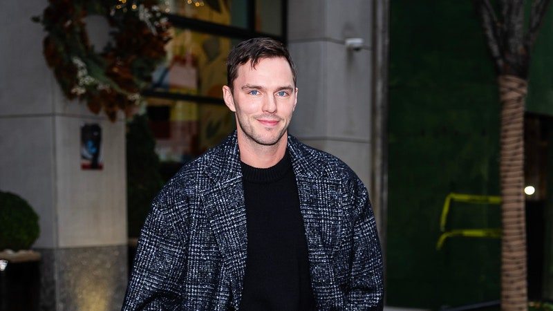 Image may contain: Nicholas Hoult, Clothing, Coat, Person, Standing, Pants, Jacket, Adult, Footwear, Shoe, Blazer, and Plant