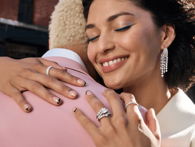 A man and woman embrace, the woman is adorned with stunning Diamond Rings and Earrings.