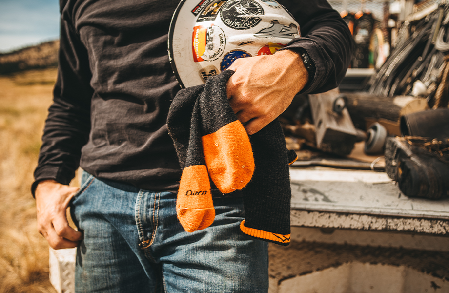 A working fellow stands outdoors with a hardhat and Darn Tough socks in hand (the essentials)