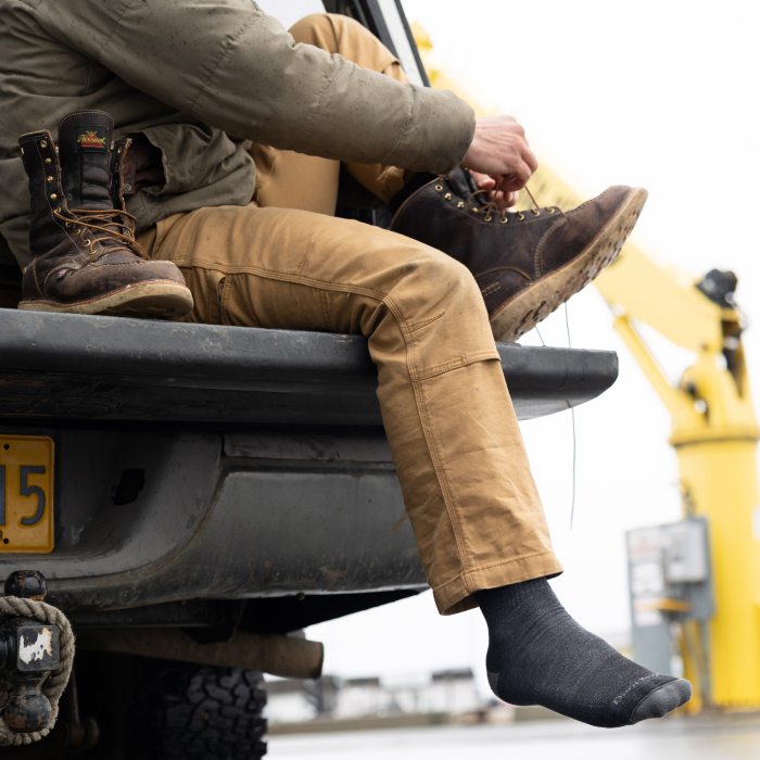 Person seated on tailgate wearing John Henry socks and tying on leather work boots