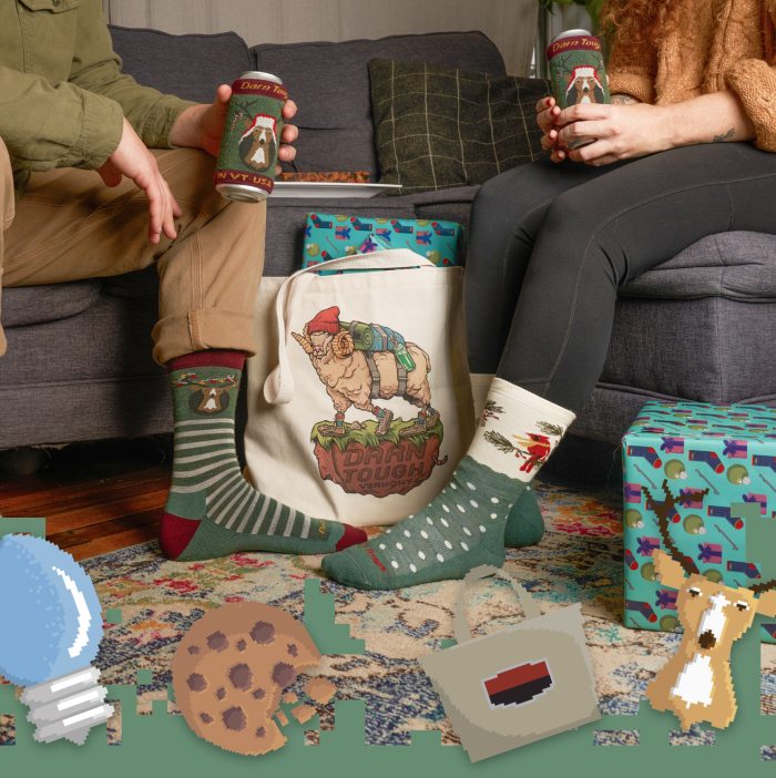 Feet wearing Darn Tough holiday socks in front of a white canvas tote bag featuring a mountain goat illustration.