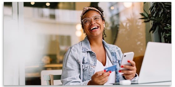 Smiling woman using a credit card and phone.