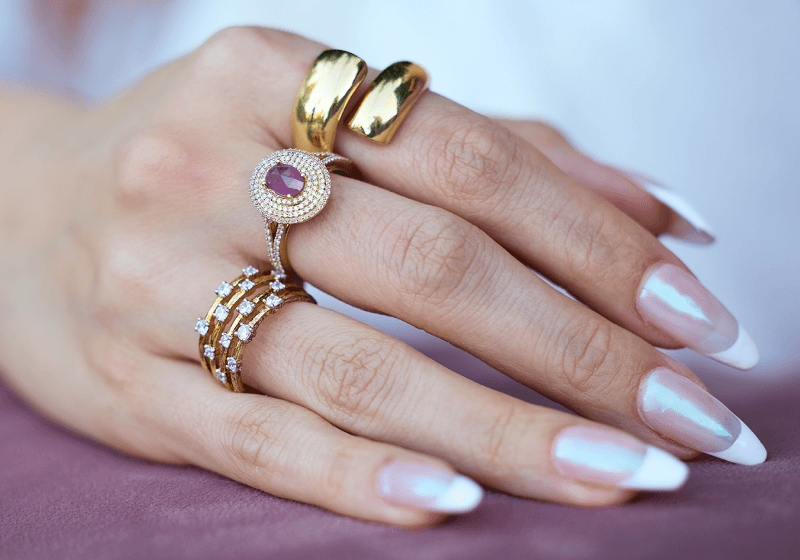 A woman poses, showcasing a variety of stunning Gold, Diamond, and Amythst Rings.