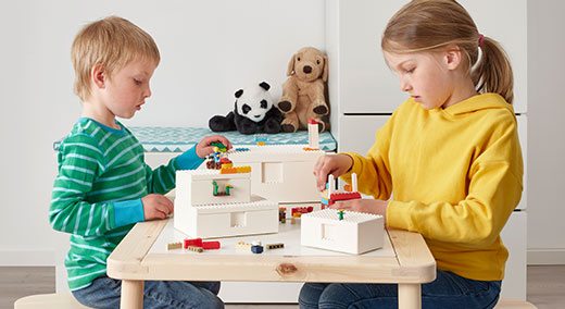 Two children play with LEGO bricks together at a wooden table